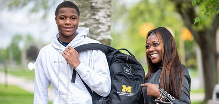 A person with a Wolverine Pathways backpack and their parent pointing at the logo