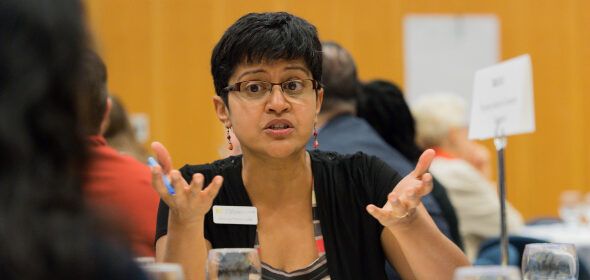 A person speaking and gesturing at a table during an event